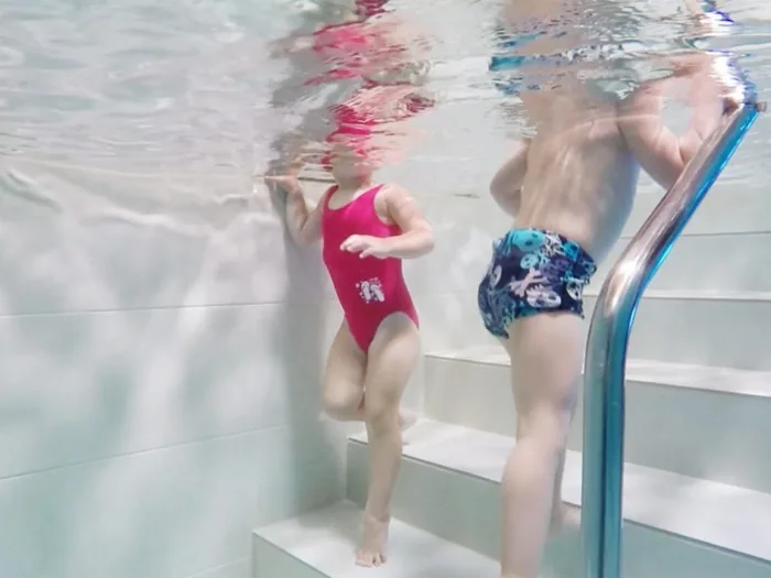 Dos infants a les escales de la piscina termal, vistos sota l'aigua