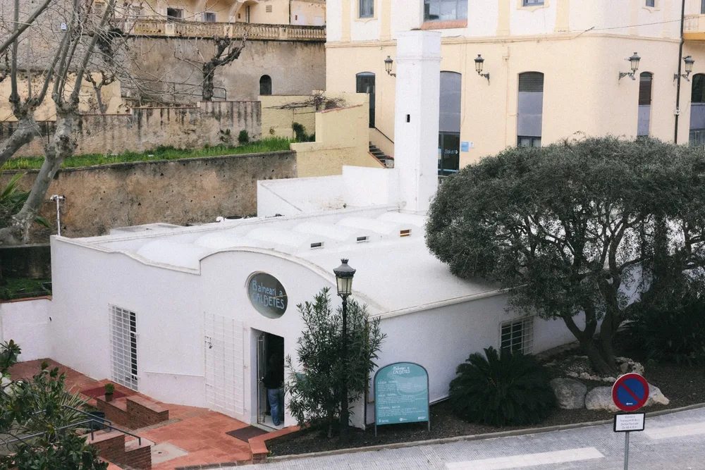 El Balneari de Caldetes vist des del carrer, amb la vila i els pins al darrere