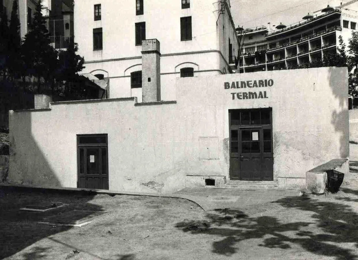 Fotografia històrica en blanc i negre de l'antic edifici del balneari, amb el rètol «BALNEARIO TERMAL» pintat a la façana