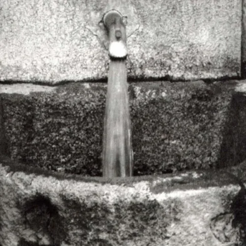 Fotografia històrica en blanc i negre de la font de pedra amb l'aigua termal rajant