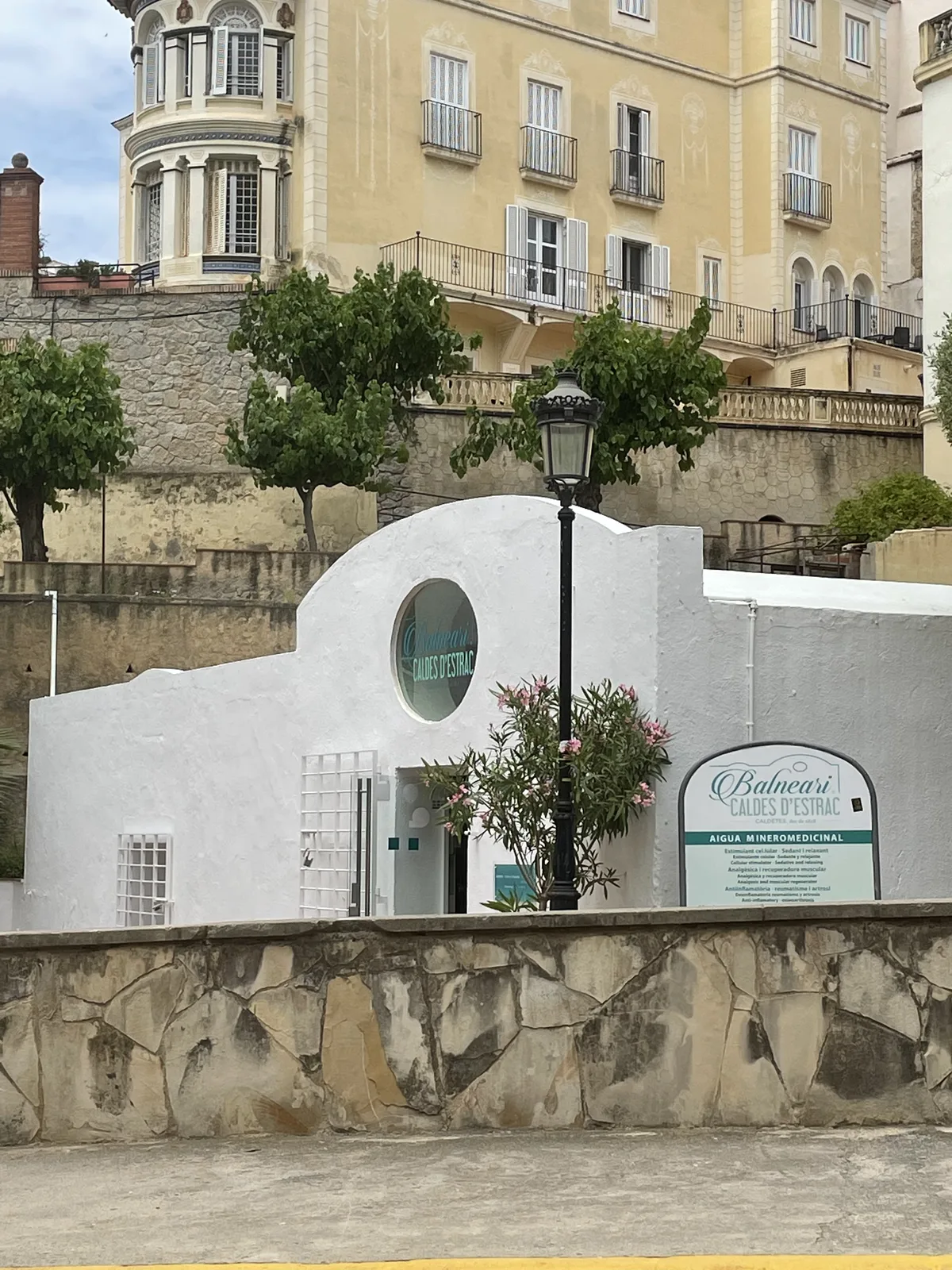 L'entrada blanca del Balneari Caldes d'Estrac, amb les cases de la vila enfilades al darrere